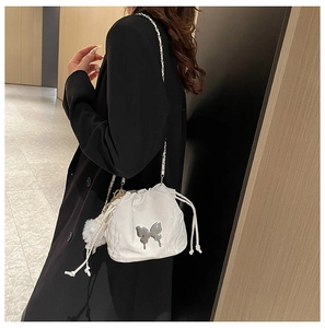 White bucket bag with silver butterfly charm and chain strap shown on model shoulder