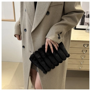 Detailed view of black plush faux fur clutch with wavy texture held by a model