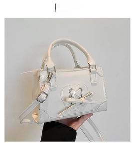 Detail of white glossy faux leather bag featuring heart-shaped lace-up and bow design