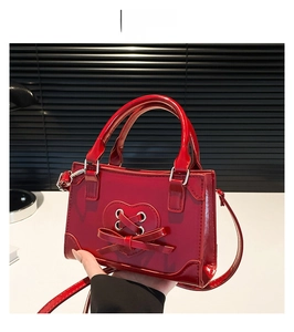 Detail of red glossy patent leather handbag with heart cutout and ribbon bow design