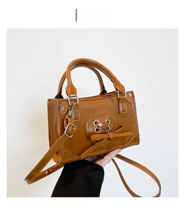 Detailed close-up of brown faux leather handbag with heart stitching and bow detail