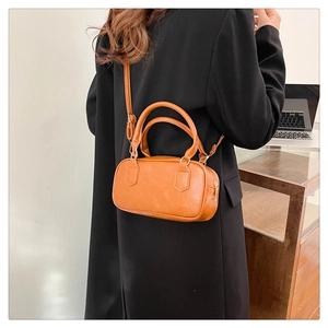 Detail view of orange vintage crossbody messenger bag worn over a black winter coat