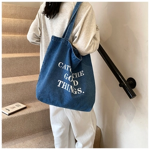 Detail of blue denim tote bag featuring white CATCH THE GOOD THINGS slogan print