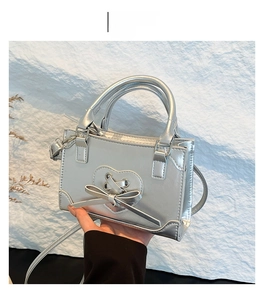 Detail of silver mini handbag featuring a decorative heart tie and metallic bow accent