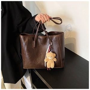 Detail view of large brown tote bag with wrinkled texture and plush bear pendant