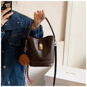 Detail of dark brown bucket bag featuring gold buckle and cute bear charm pendant