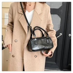 Detail of a minimalist black Boston handbag with shiny gold hardware and shoulder strap