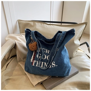Detail of blue denim tote bag with white lettering and cute brown bear pendant accessory