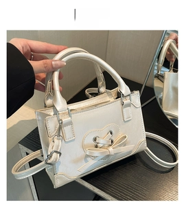 Detail view of pearly white handbag featuring a heart-shaped lace-up bow and silver hardware