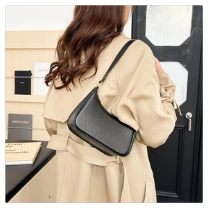 Sleek black minimalist baguette bag with glossy finish styled over a beige trench coat