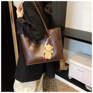 Detail of dark brown tote bag on shoulder with plush bear charm and glossy finish