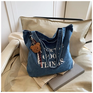 Detail of denim tote bag with letter print and a cute plush bear charm on a seat