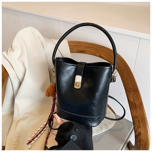 Detail view of black textured bucket bag with golden twist lock and decorative charm