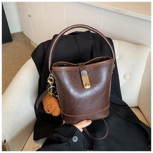 Detail of vintage textured dark brown bucket bag with gold clasp and plush bear charm