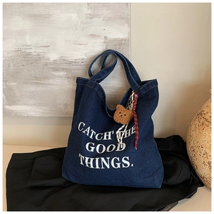 Detail showing deep blue denim tote with white letter print and brown bear charm