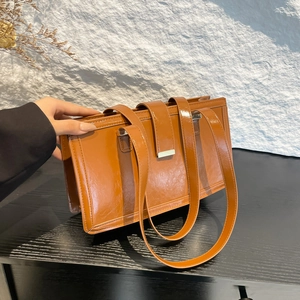 Minimalist brown vintage oil wax leather shoulder bag with sleek metal buckle on a black desk