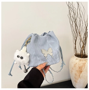 Detail of light blue bucket bag with metallic butterfly and plush monster charm