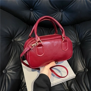 Classic wine red Boston bag in glossy leather held against a dark aesthetic backdrop