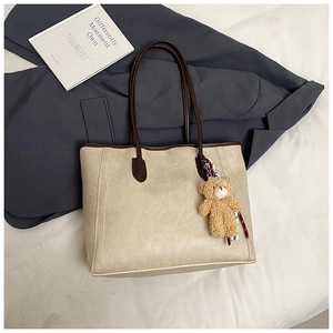 Detailed view of beige tote bag with brown straps and cute plush bear accessory
