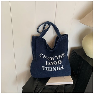 Detail of blue denim tote bag with white 'CATCH THE GOOD THINGS' printed lettering