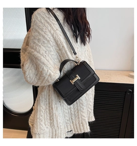 Close-up of black matte leather shoulder bag with gold H-clasp on model in cozy interior