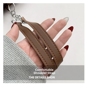 Close-up of brown leather shoulder strap with orange stitching and silver metal chain link