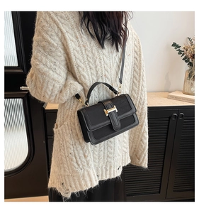 Detail of a black leather crossbody bag featuring a golden H-shaped clasp and top handle
