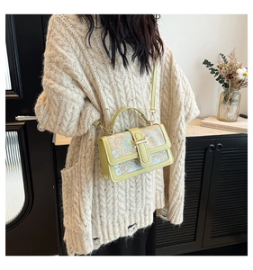 Detail of light green crossbody bag with floral fabric panel and gold clasp closure