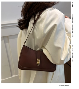 Close-up of dark brown minimalist leather underarm bag with gold metal buckle clasp