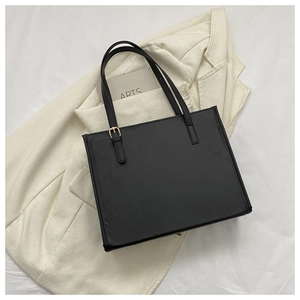 Flat lay of minimalist black tote bag with gold buckle on white bedding and blazer