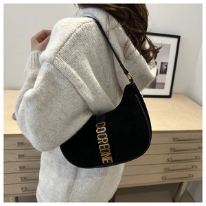 Détail du sac demi-lune en daim noir avec lettres dorées porté à l'épaule par un mannequin