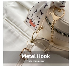 Detail of light gold hardware hooks and patterned silk scarf on cream cylinder bag