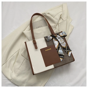 Detail of color-block tote bag with FASHION logo and elegant floral scarf on handle