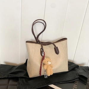 Minimalist cream tote bag with brown straps and cute plush bear charm on leather coat
