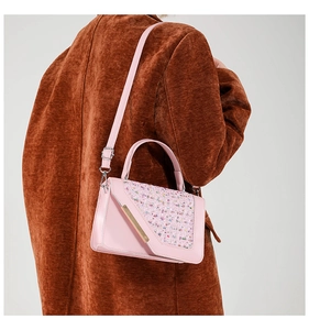 Close-up of pink houndstooth crossbody bag with golden metal lock on a model's coat