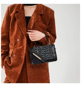 Detail of a chic black bag with a colorful tweed flap and gold metal buckle accents