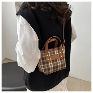 Dettaglio della borsa tote vintage a quadri con manici in pelle indossata da una modella