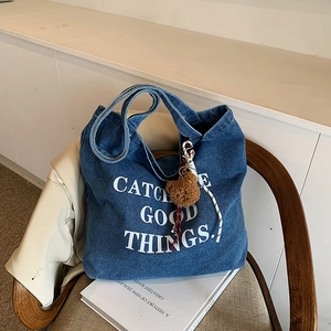 Blue denim tote bag with letter print and teddy charm on a chair for daily commute