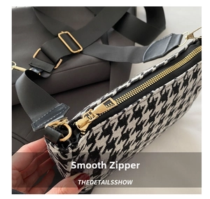 Close-up of a smooth metal zipper on a black and white houndstooth pattern crossbody bag