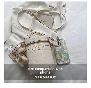Detail view of crocodile pattern barrel bag with silk scarf handle and bear charm decoration