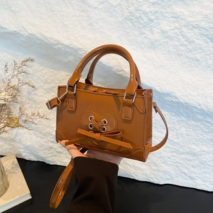 Caramel brown vintage crossbody bag with heart strap and bow detail on studio background