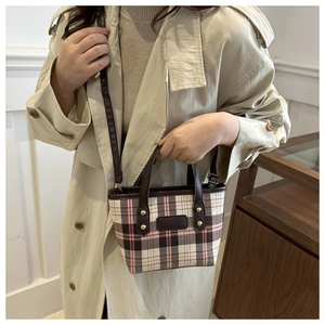 Dettaglio borsa a quadri rosa e marrone con manici in pelle indossata su trench beige