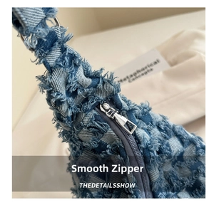 Close-up of blue checkerboard denim bag showing smooth metal zipper and frayed edge texture