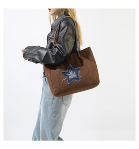 Detail of suede tote bag with denim star patch and leather strap worn by a model