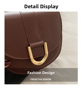 Detail of brown leather saddle bag featuring a large gold U-shaped buckle and fine stitching