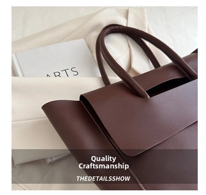 Detail of dark brown leather tote bag with lychee texture and rounded handle on white blazer