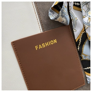 Detail of brown leather pouch with gold fashion text and stitched edges on a scarf background