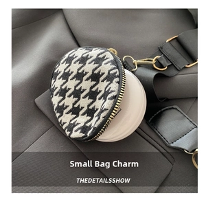 Close-up of houndstooth mini coin purse with gold zipper and clip on grey fabric