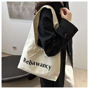 Detail of cream canvas tote bag featuring side drawstring bow and black text print