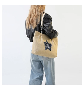 Shoulder shot of khaki suede tote bag with blue star patch and white straps on model